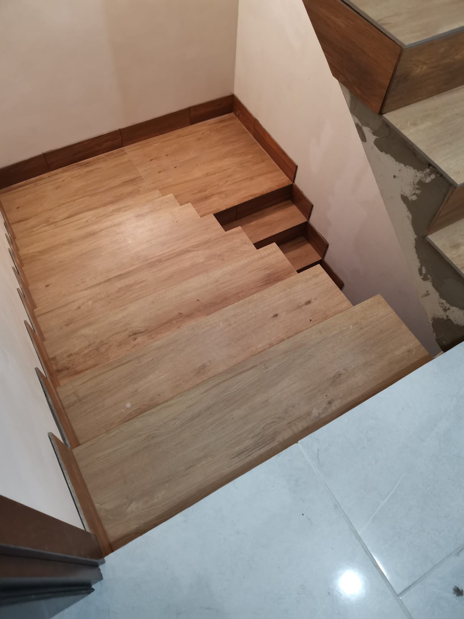 Wykończone drewnopodobną płytką schody w domu w Sulejówku, widoczne fragmenty ściany i podłogi z jasnych płytek.