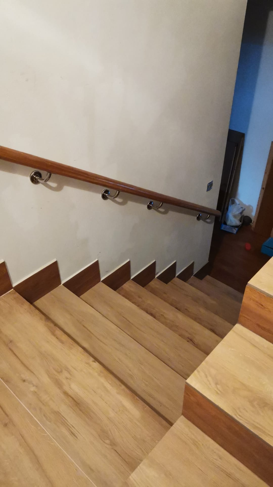 Schody wyłożone panelami drewnopodobnymi z zamontowaną drewnianą poręczą z metalowymi uchwytami, widok z góry w dół.