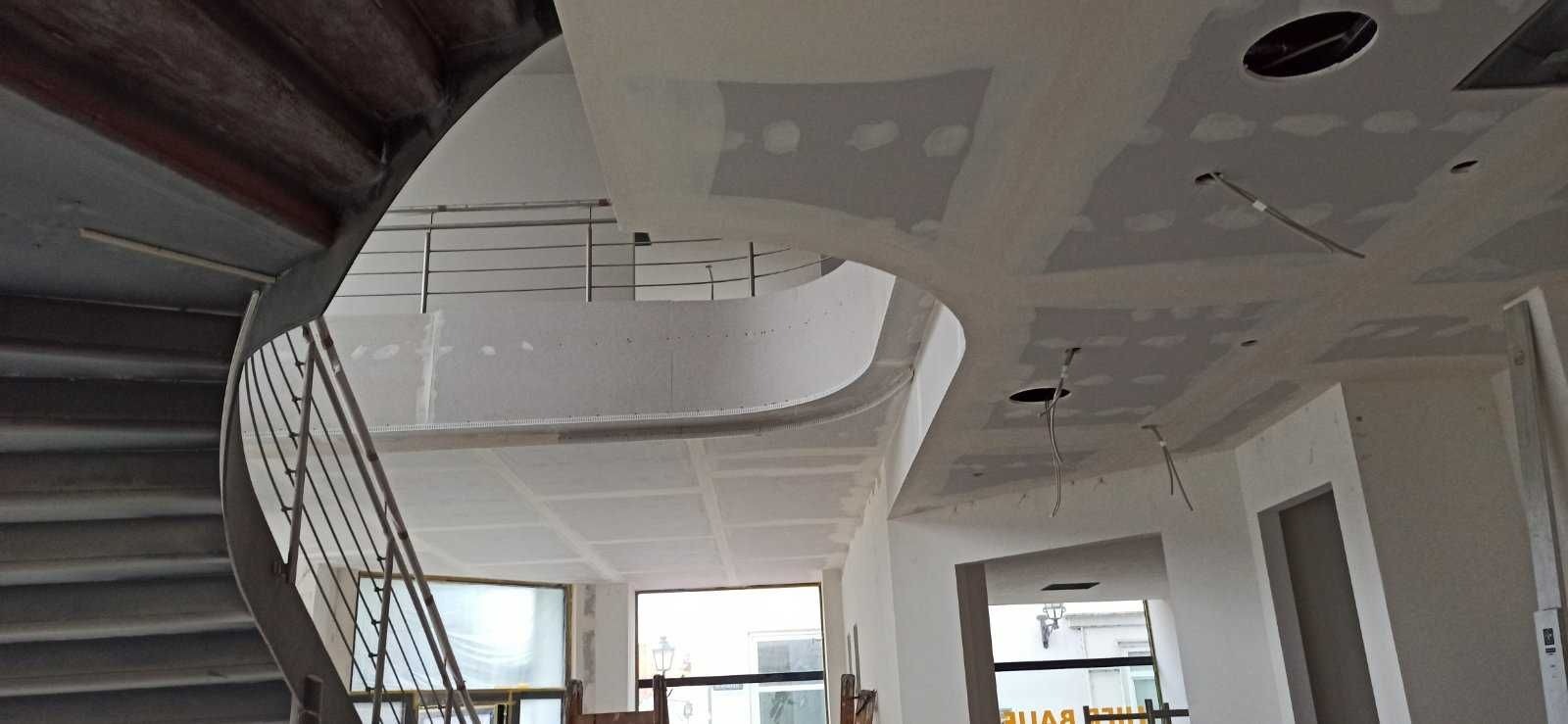 Wnętrze w trakcie prac wykończeniowych: widoczna spiralna klatka schodowa, sufit z płyt gipsowo-kartonowych przed szpachlowaniem, z widocznymi otworami na oświetlenie i przewodami.