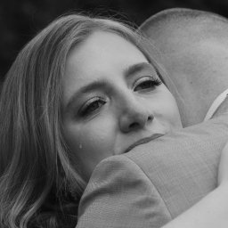 Marta Jasiukiewicz Fotografia - Czarno-białe zbliżenie kobiety z łzą w oku, obejmującej mężczyznę w garniturze. Ujęcie z uroczystości, skupione na emocjach i detalu twarzy.