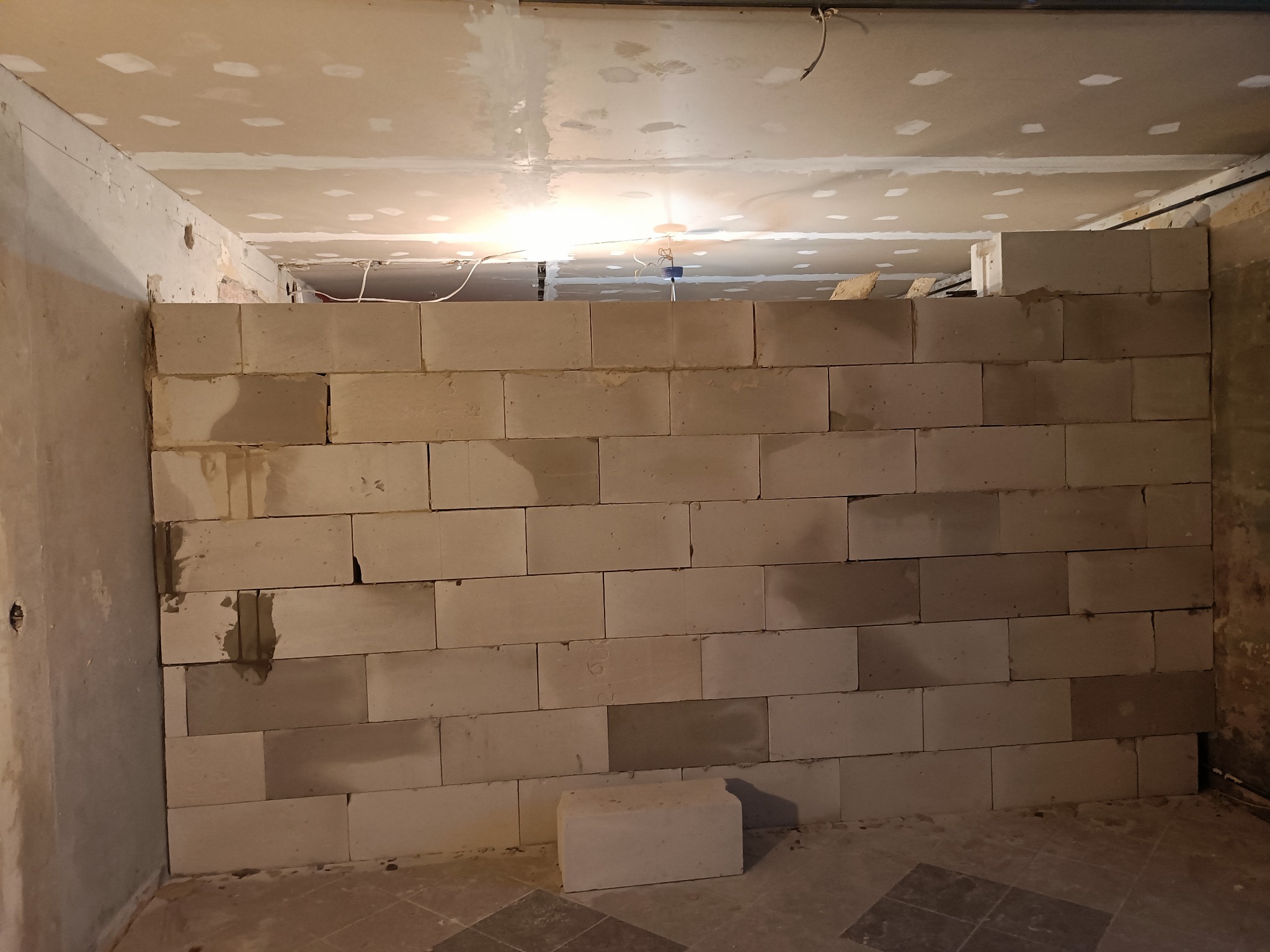 Wznoszenie ściany działowej z bloczków betonu komórkowego w surowym wnętrzu, widoczne niedoskonałości na suficie przygotowanym pod wykończenie.