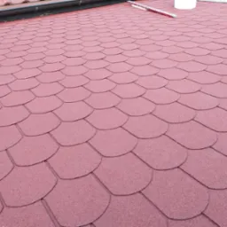 Czerwony dach pokryty gontem bitumicznym w kształcie rybiej łuski, widoczny fragment rynny i poziomicy.