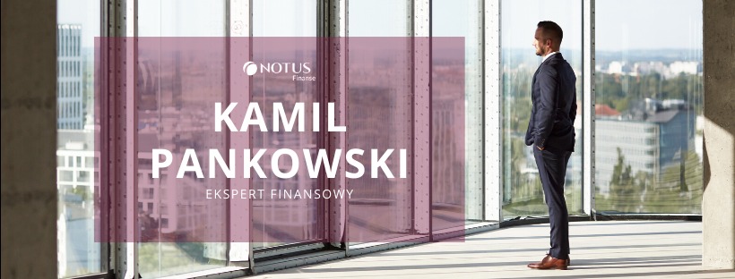 Mężczyzna w garniturze, Kamil Pankowski, ekspert finansowy Notus Finanse, patrzy przez okno na panoramę miasta. Minimalistyczne wnętrze z betonowym filarem.