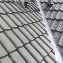 Żarbud - Prace dekarskie: Montaż szarej dachówki ceramicznej na dachu przez dekarzy, widoczne narzędzia i elementy konstrukcji dachu.