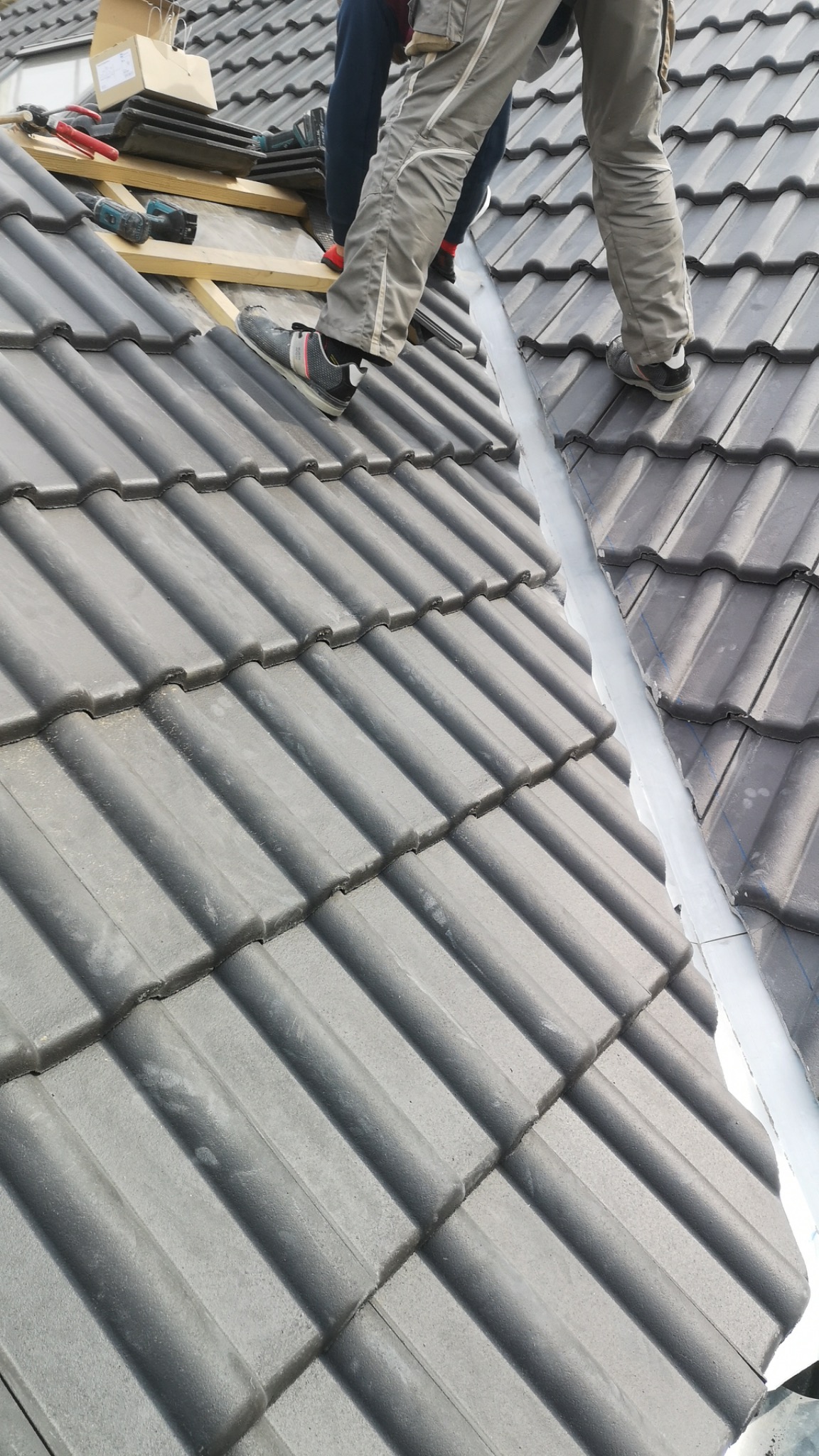 Prace dekarskie: Montaż szarej dachówki ceramicznej na dachu przez dekarzy, widoczne narzędzia i elementy konstrukcji dachu.