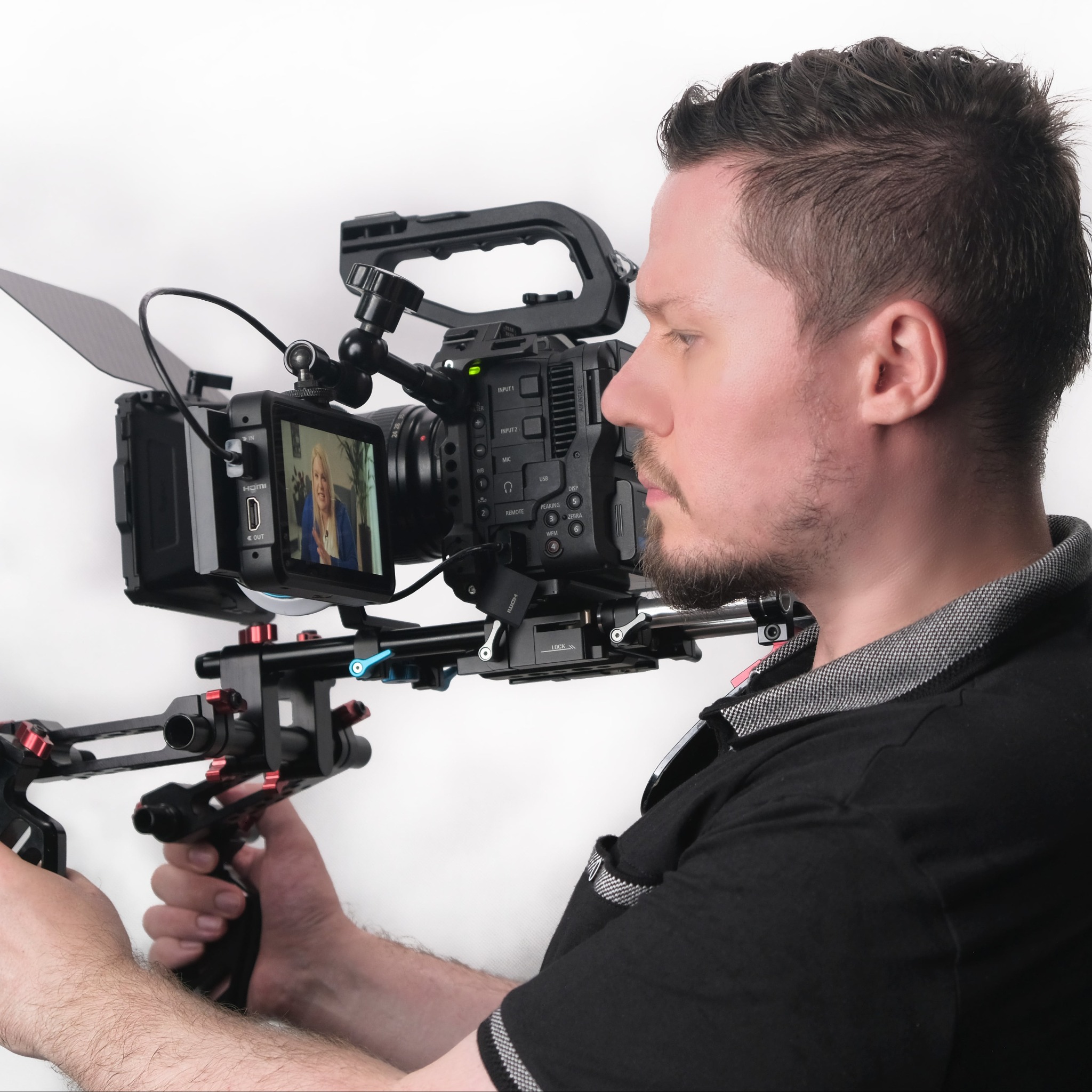 Operator filmowy trzymający profesjonalną kamerę filmową z zamontowanym rigiem, ekran kamery pokazuje nagrywaną osobę.