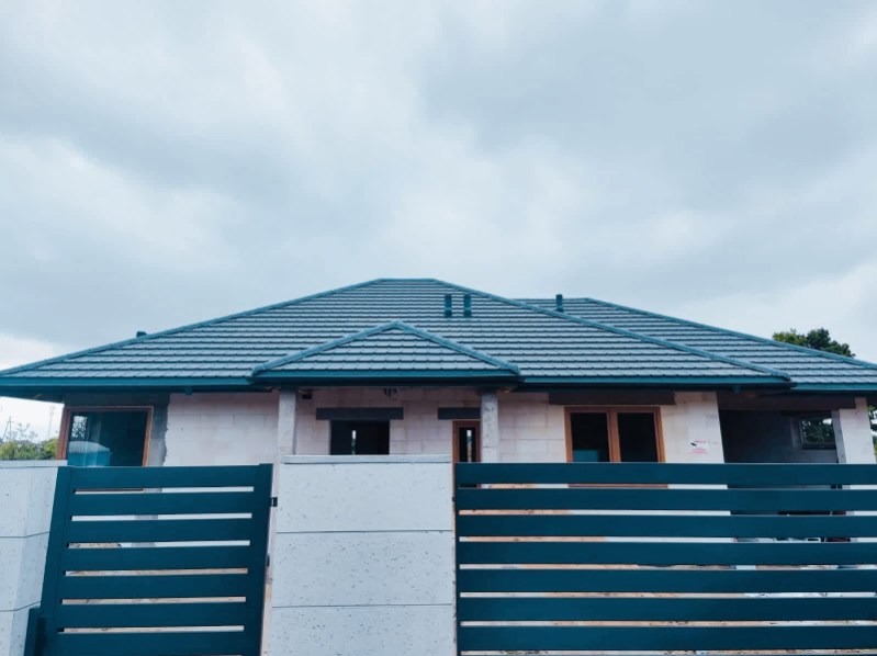 Dom jednorodzinny z szarą dachówką karpiówką i nowoczesnym ogrodzeniem panelowym. Widok z zewnątrz, pochmurne niebo w tle.