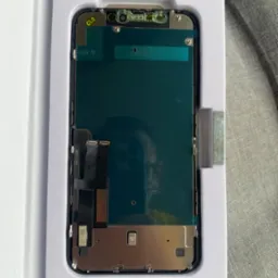 Nowy ekran iPhone w opakowaniu, widoczne złącza i elementy montażowe, naklejka 'CLG' w lewym górnym rogu.