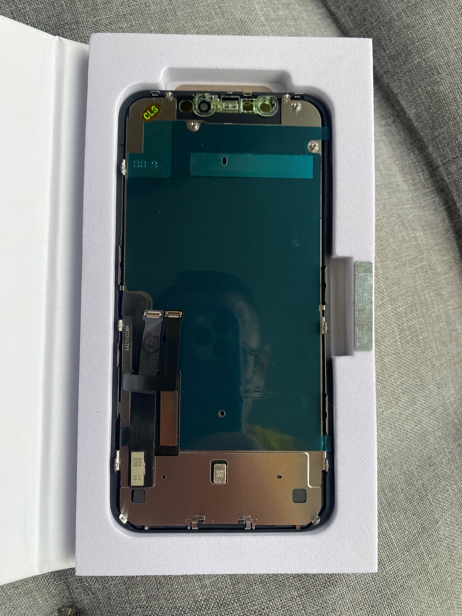 Nowy ekran iPhone w opakowaniu, widoczne złącza i elementy montażowe, naklejka 'CLG' w lewym górnym rogu.