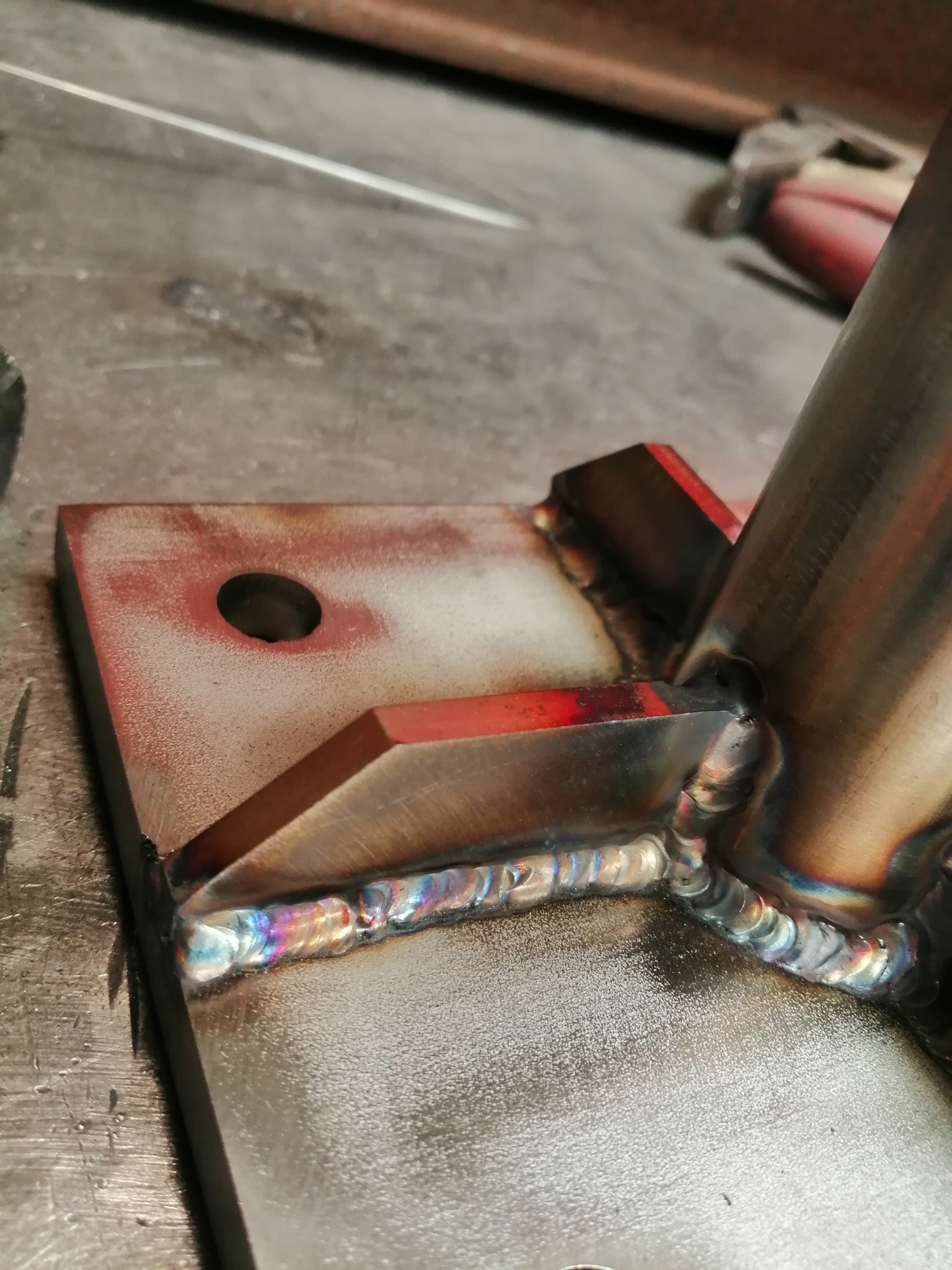 Szczegółowe zbliżenie na spawany element konstrukcyjny z metalu, widoczne tęczowe przebarwienia na spoinie.