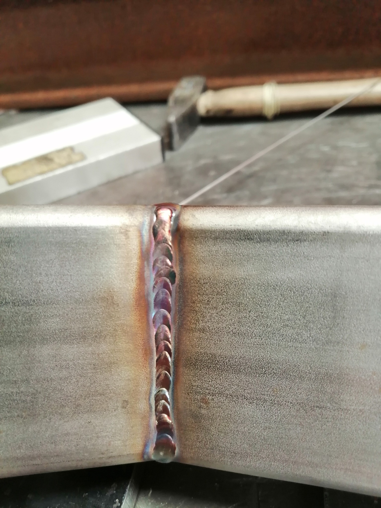 Zbliżenie na świeżo wykonany spaw na profilu metalowym, widoczne charakterystyczne przebarwienia termiczne i ślady obróbki.