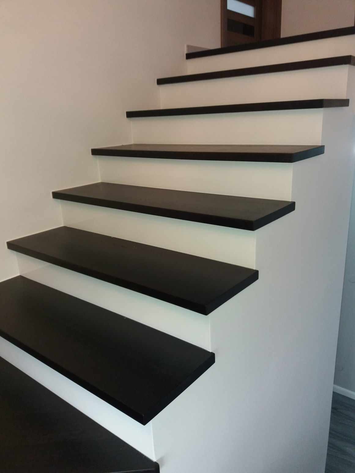 Nowoczesne schody z czarnymi stopniami i białymi podstopnicami, widok z dołu, minimalistyczny design, drzwi w tle.