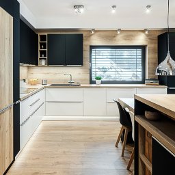 Proste Formy Anna Wojtyłko - Nowoczesna kuchnia z drewnianymi i czarnymi szafkami, białymi blatami, podświetleniem LED pod szafkami i wyspą kuchenną z drewnianym blatem.