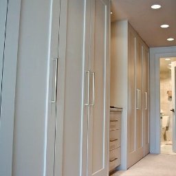 Proste Formy Anna Wojtyłko - Biała szafa wnękowa z długimi srebrnymi uchwytami, widoczna z perspektywy korytarza z otwartymi drzwiami do łazienki.