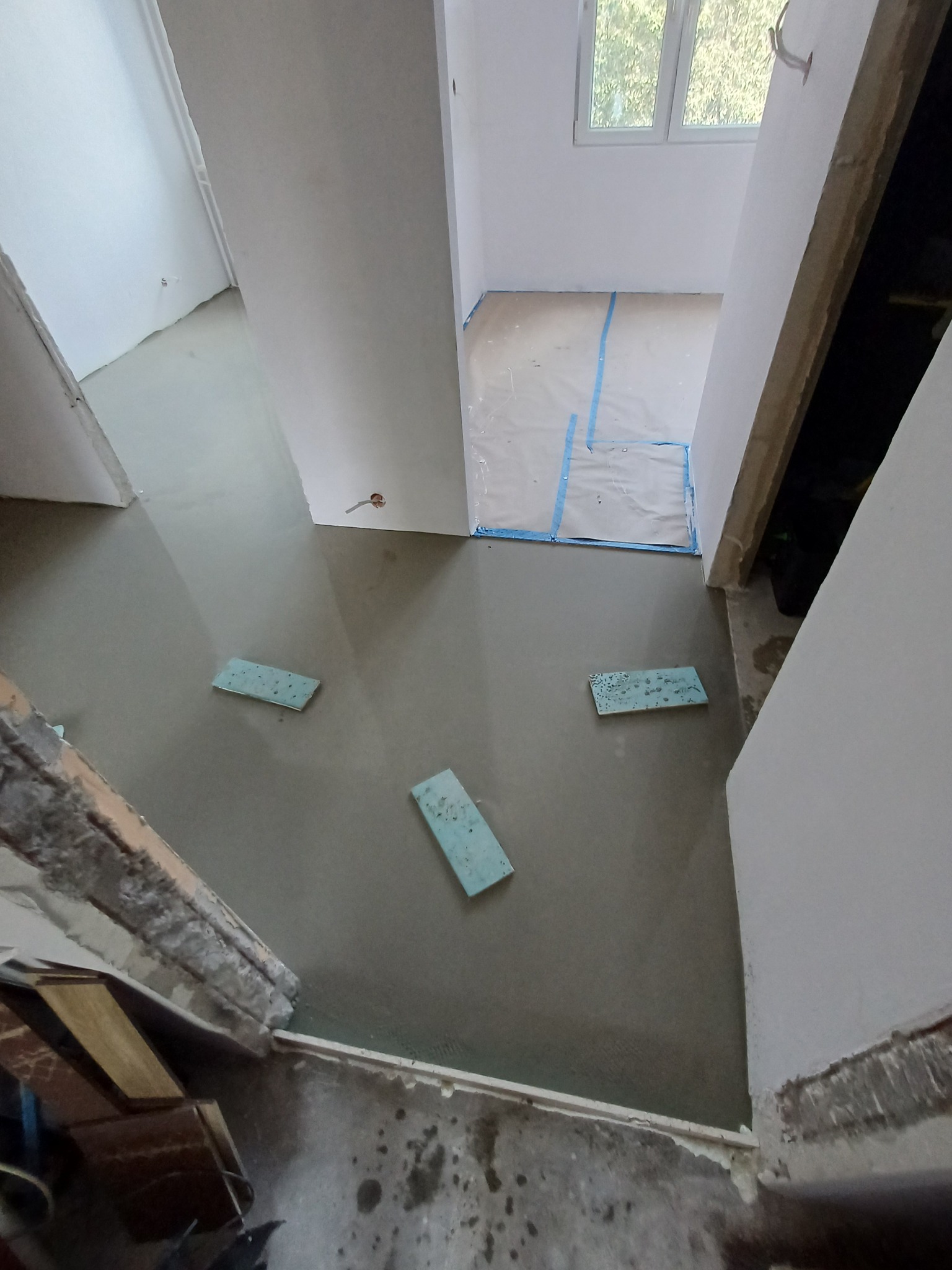 Wylewka samopoziomująca w trakcie prac, widoczne fragmenty pianki dylatacyjnej i przygotowane pomieszczenie z oknem. Ujęcie z góry, surowy stan.