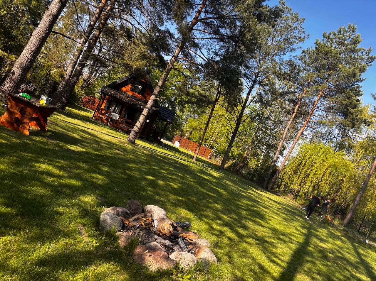 Urokliwy ogród z domkiem w stylu rustykalnym i paleniskiem w Markach. Zieleń, drzewa i elementy architektury krajobrazu tworzą harmonijną całość.