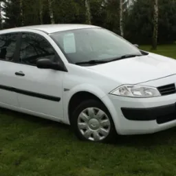 Biały Renault Megane II na trawniku przed domem, widoczna kartka z ceną za szybą.