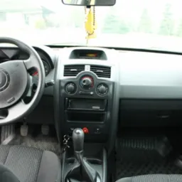 Wnętrze Renault Megane II z widoczną deską rozdzielczą, kierownicą z logo Renault oraz zawieszką zapachową na lusterku.