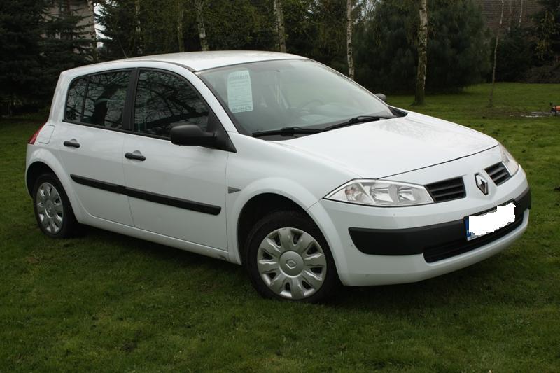 Biały Renault Megane II na trawniku przed domem, widoczna kartka z ceną za szybą.