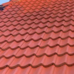 Czerwona dachówka ceramiczna ułożona na dachu w słoneczny dzień, widok z dołu pod kątem.