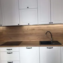 Białe szafki kuchenne z drewnianym blatem i czarnym zlewem w Hucie Krzeszowskiej, widoczne detale wykończenia frontów.