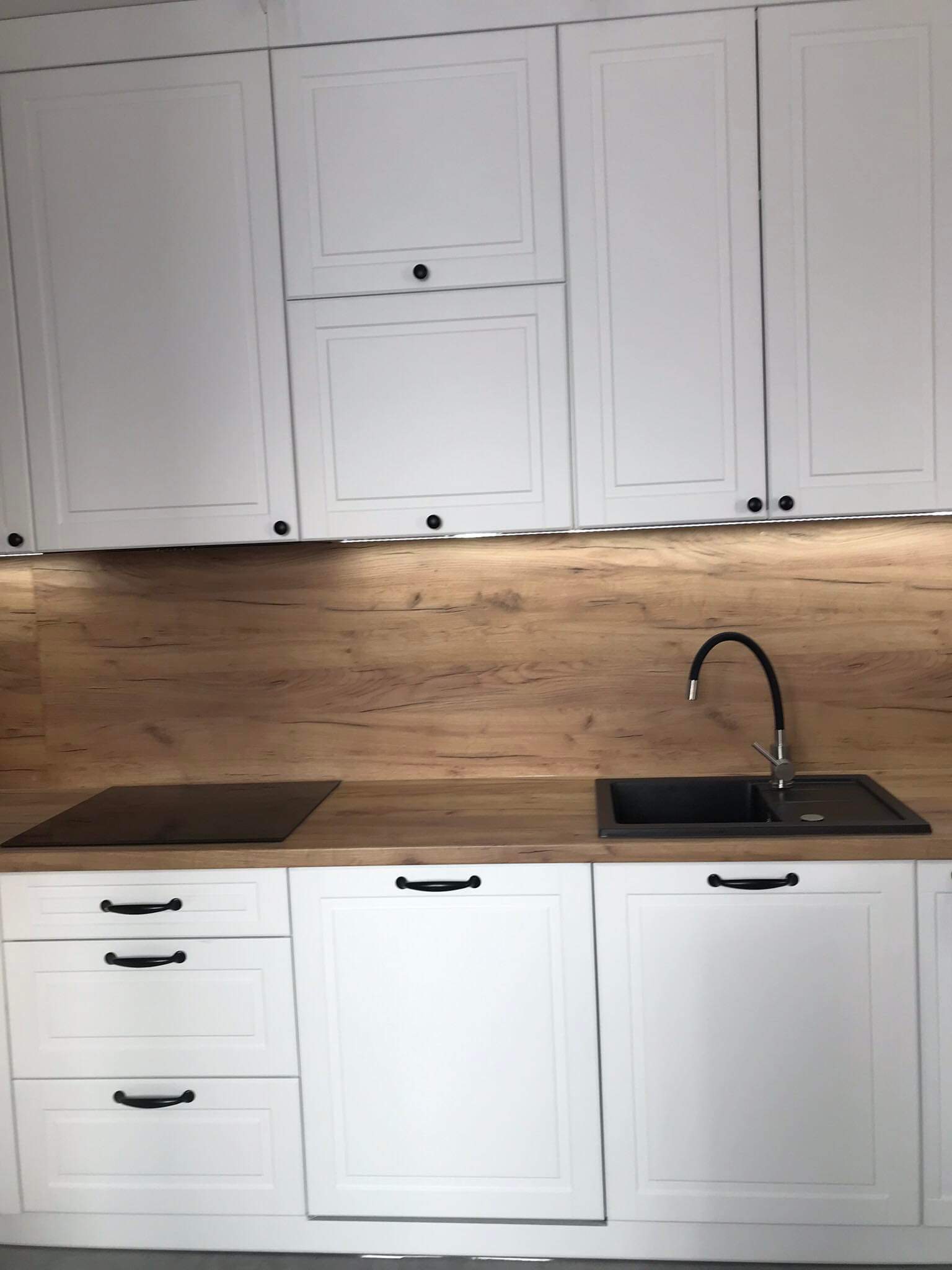 Białe szafki kuchenne z drewnianym blatem i czarnym zlewem w Hucie Krzeszowskiej, widoczne detale wykończenia frontów.