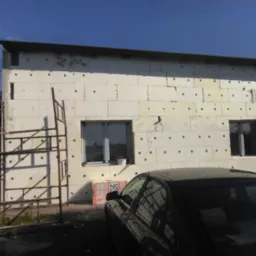 Ocieplanie elewacji budynku styropianem, widoczne rusztowanie i zaparkowany samochód