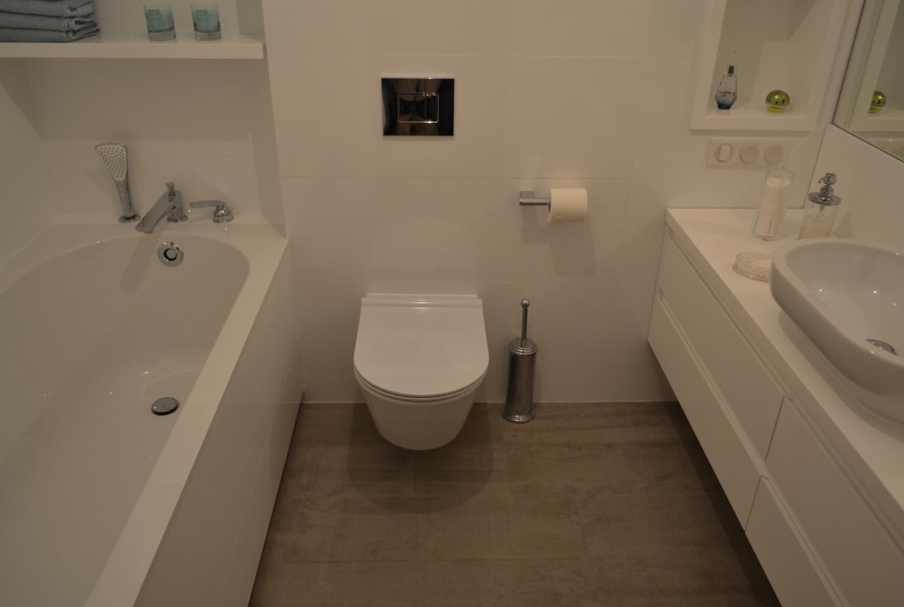 Nowoczesna, biała łazienka z wanną, umywalką nablatową i toaletą. Minimalistyczny design, płytki w odcieniach beżu na podłodze. Funkcjonalne i estetyczne wykończenie.