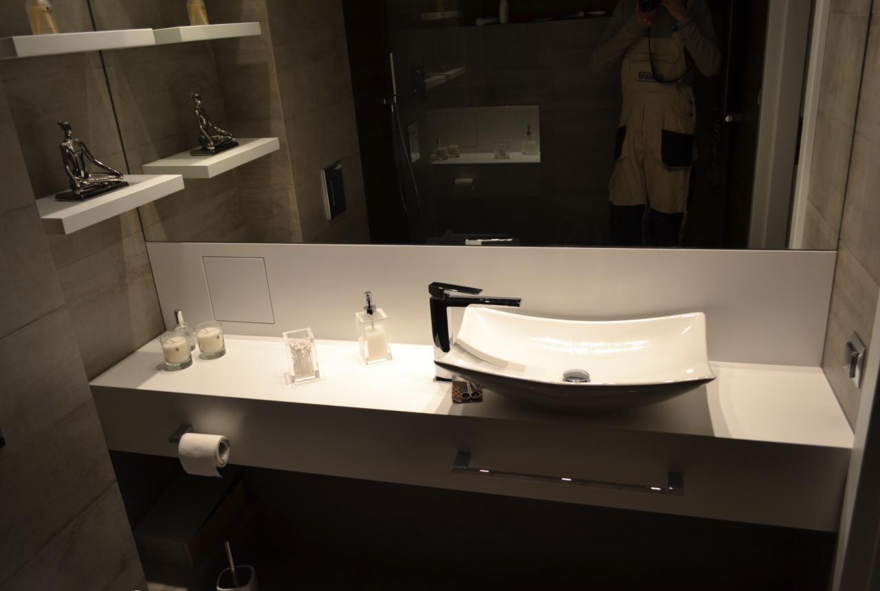 Nowoczesna łazienka z umywalką w kształcie łodzi, minimalistyczne półki z dekoracjami i odbicie osoby robiącej zdjęcie w dużym lustrze.