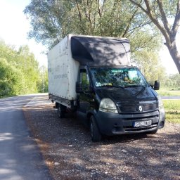 Zaki Trans - Czarny bus Renault Master z plandeką, zaparkowany na poboczu drogi w otoczeniu drzew. Na plandece widoczny napis reklamowy, a na desce rozdzielczej pluszowe zabawki.
