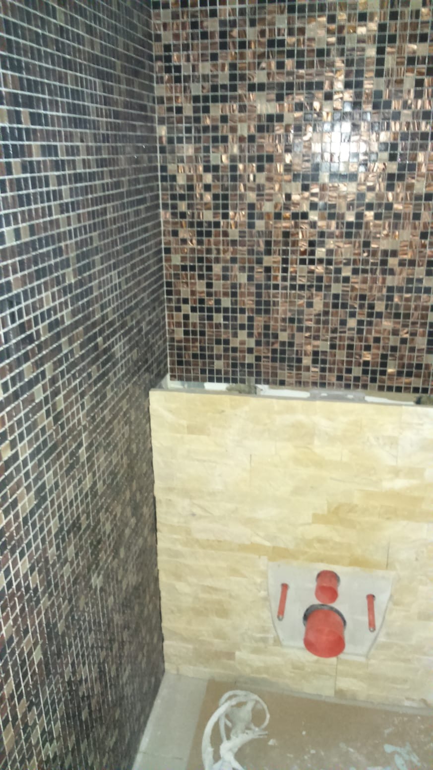 Mozaika ścienna w odcieniach brązu i beżu w łazience, z widoczną instalacją podtynkową WC.