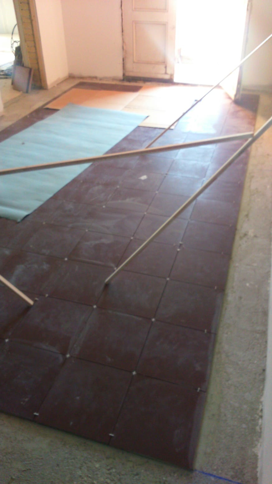 Przygotowanie podłoża pod posadzkę w Kielcach: brązowe, kwadratowe płyty rozłożone na podkładzie, widoczne listwy poziomujące i częściowo zakryta folią podłoga.