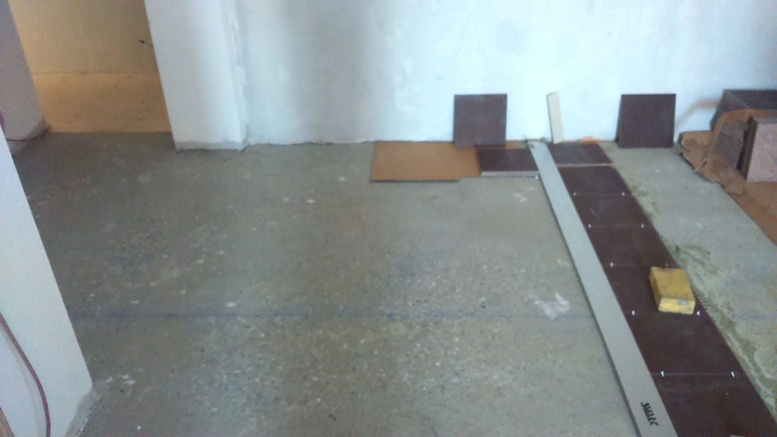 Przygotowanie podłoża pod płytki: wyrównana wylewka, przymiarka płytek, listwa wyrównująca i poziomica w pomieszczeniu przed remontem.