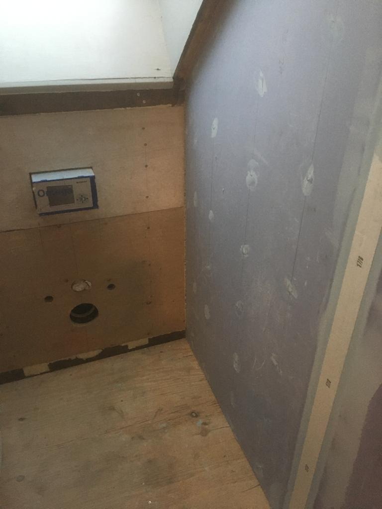 Surowa ściana z płyt gipsowo-kartonowych, przygotowana do dalszych prac wykończeniowych, widoczne ślady po szpachlowaniu w miejscach łączeń płyt, zarys instalacji elektrycznej.