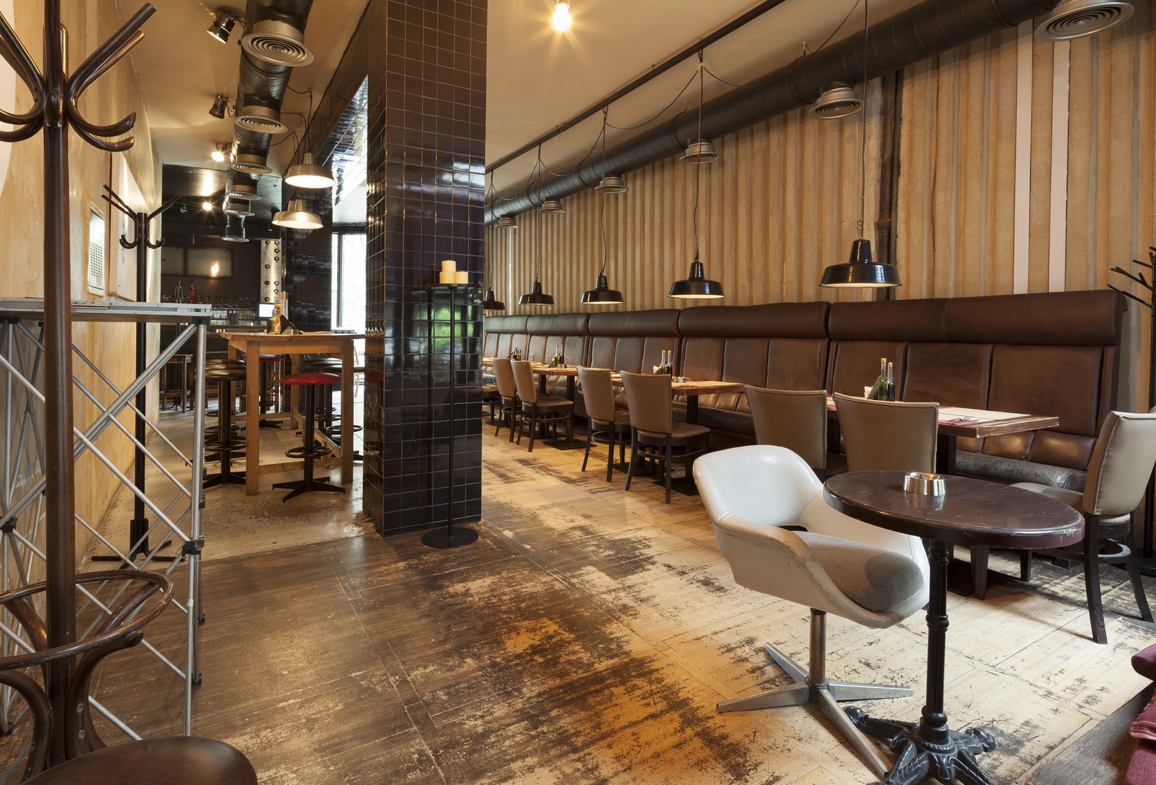 Wnętrze restauracji z długą, skórzaną kanapą, stolikami z krzesłami, kolumną z ciemnych płytek i podłogą imitującą stare drewno.