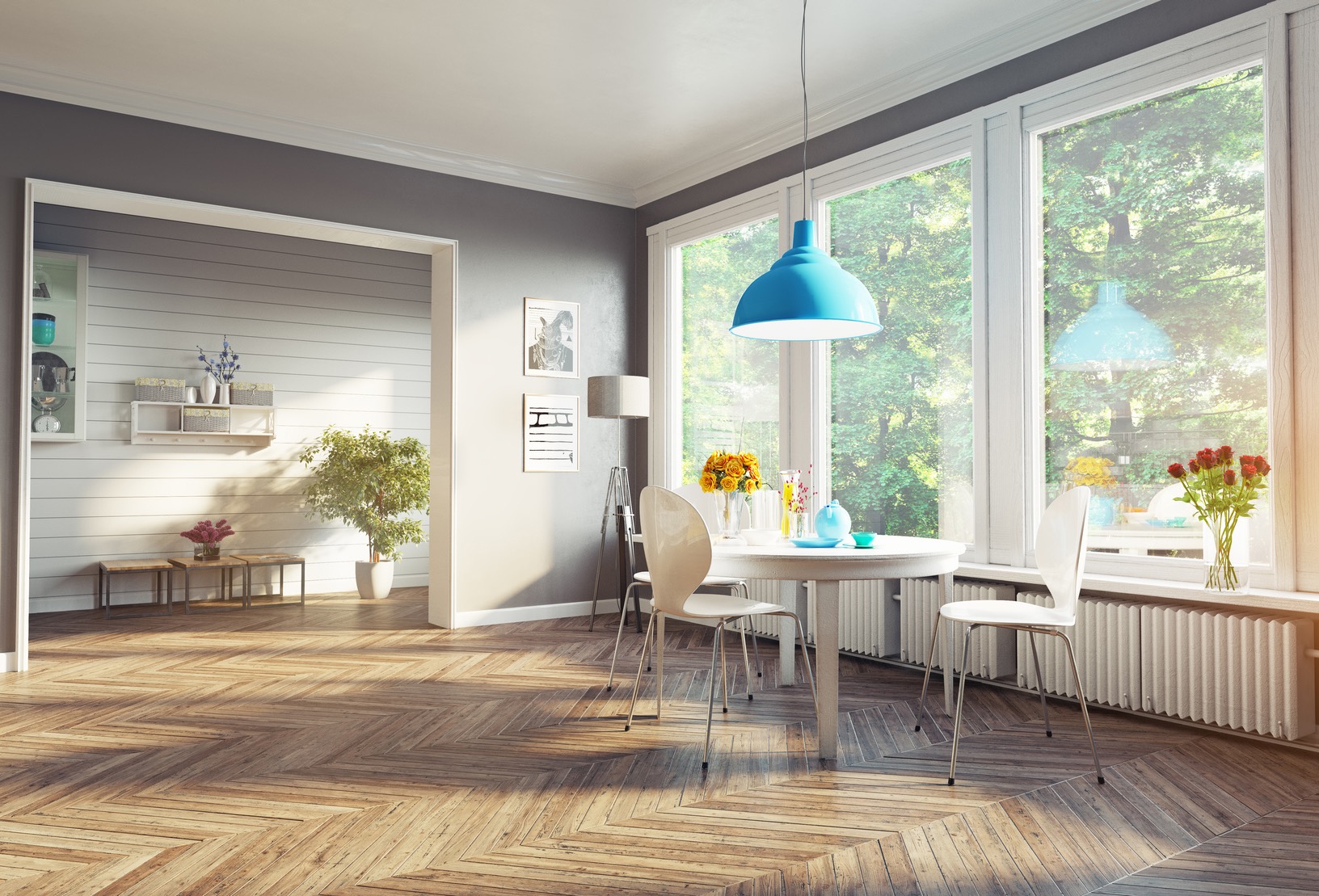 Jasne wnętrze jadalni z parkietem w jodełkę, białym okrągłym stołem, krzesłami i turkusową lampą wiszącą; widok na zieleń za oknem.