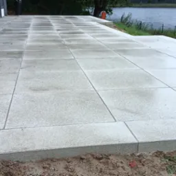 Nowoczesny taras z betonowych płyt w odcieniach szarości, z widokiem na jezioro w tle, świeżo obsypany ziemią.