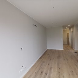 Farmont Gabriel Faryna - Wnętrze w Poznaniu po remoncie: świeżo pomalowane ściany w odcieniach szarości, jasna drewniana podłoga z widocznymi słojami, przygotowane otwory na gniazdka elektryczne i fragment schodów...