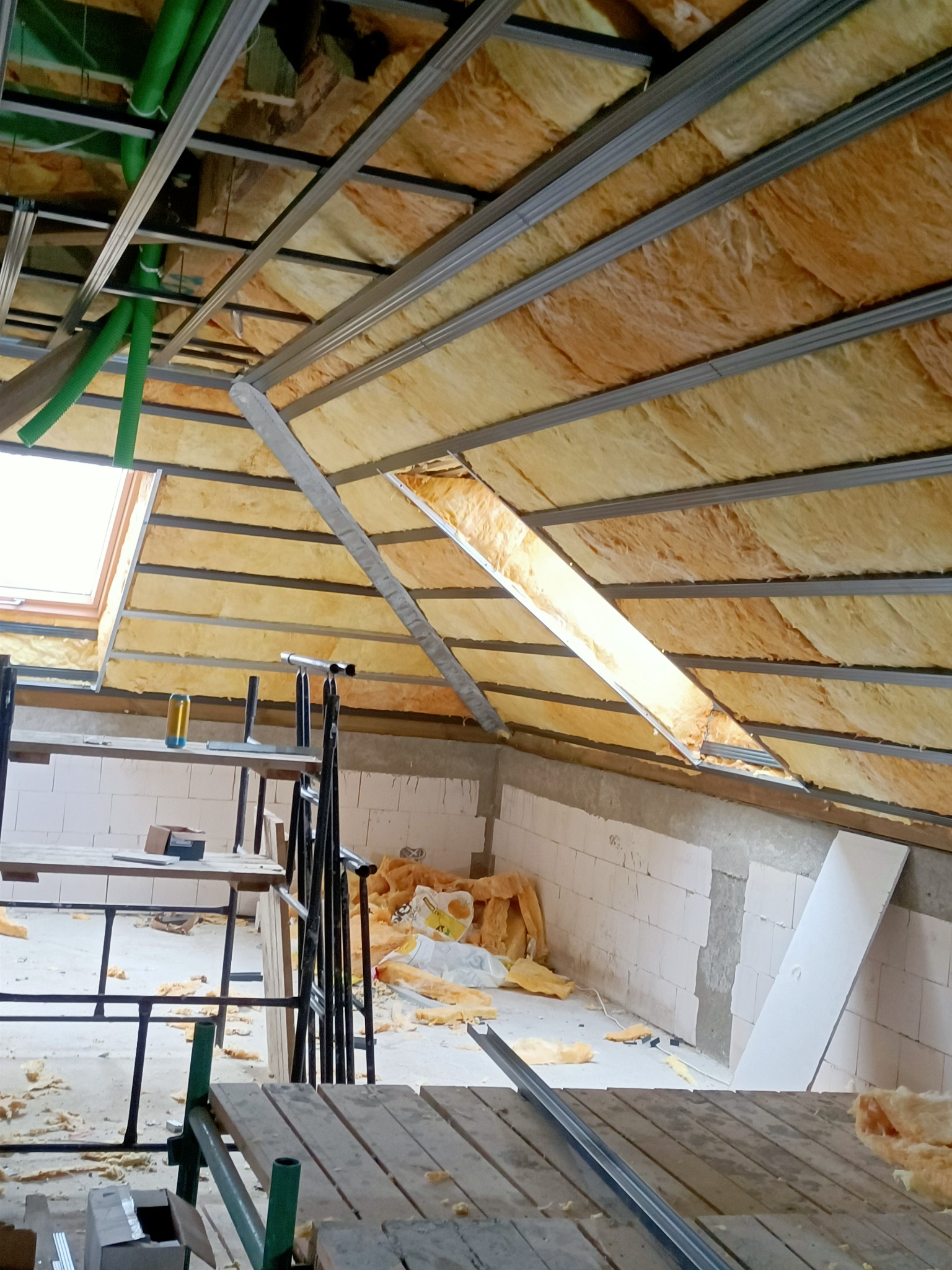 Montaż izolacji z wełny mineralnej na poddaszu w Szczecinie, widoczne metalowe profile sufitowe i fragment okna dachowego.