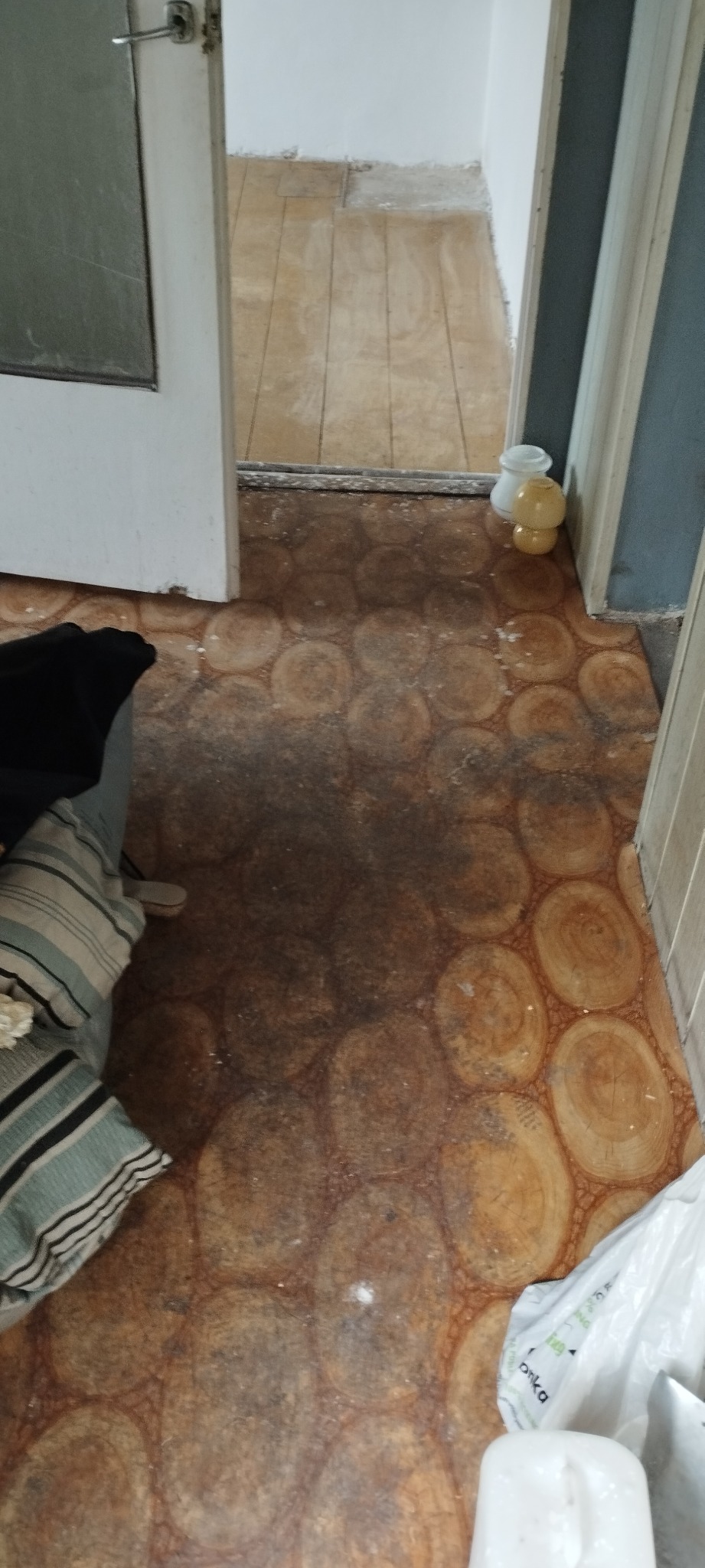 Podłoga z wzorem imitującym przekrój pnia drzewa, widoczne zabrudzenia i resztki po remoncie, w tle fragmenty mebli i drzwi
