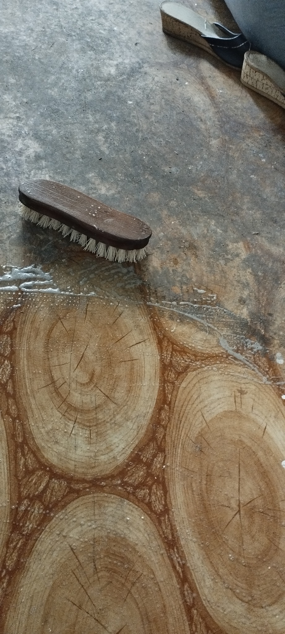 Szczotka do szorowania podłogi z drewnopodobnym wzorem, widoczne resztki wody i detergentu.