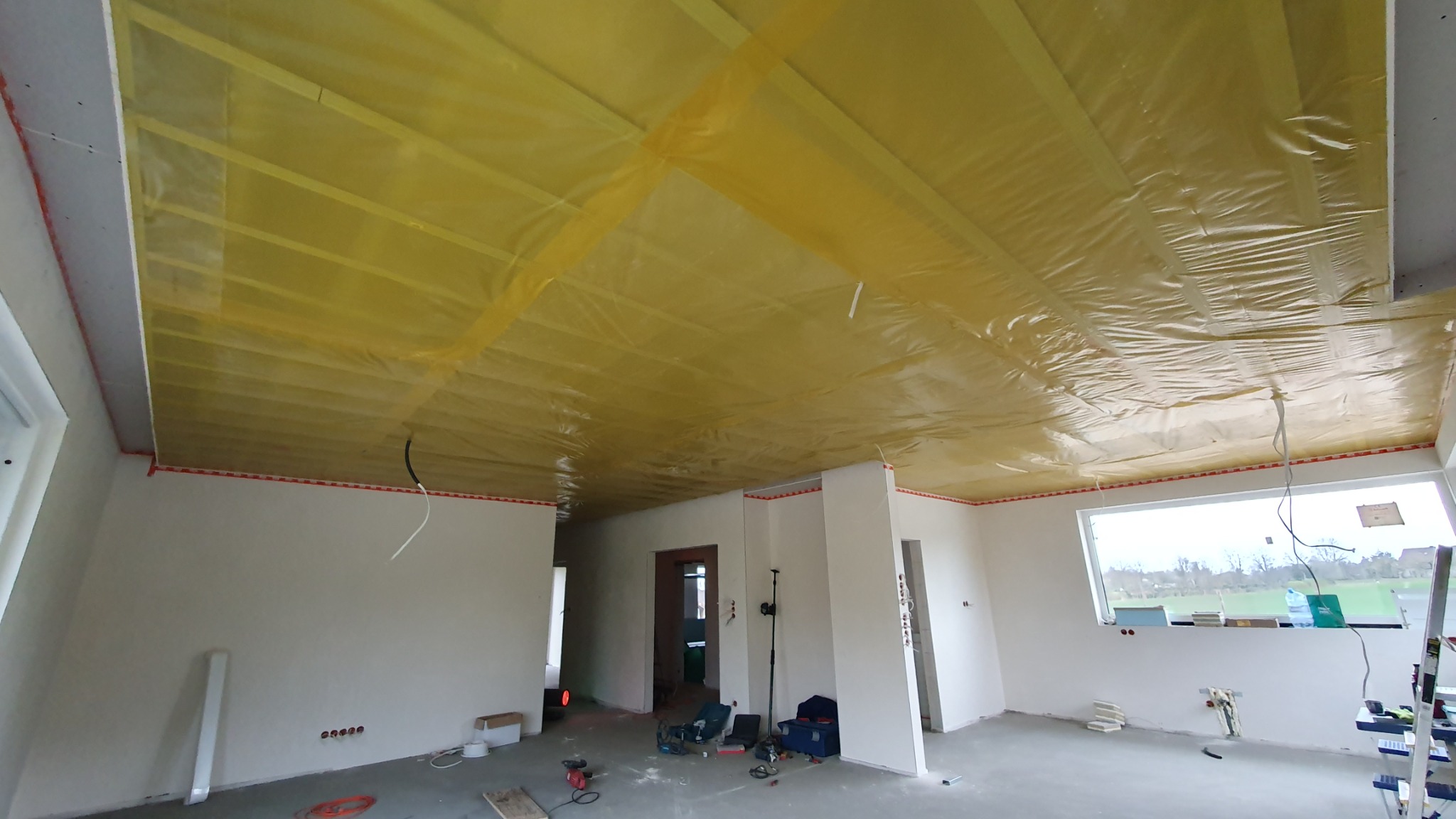 Wnętrze w trakcie prac wykończeniowych: sufit zabezpieczony folią malarską, ściany przygotowane do dalszych prac, widoczne narzędzia na podłodze.