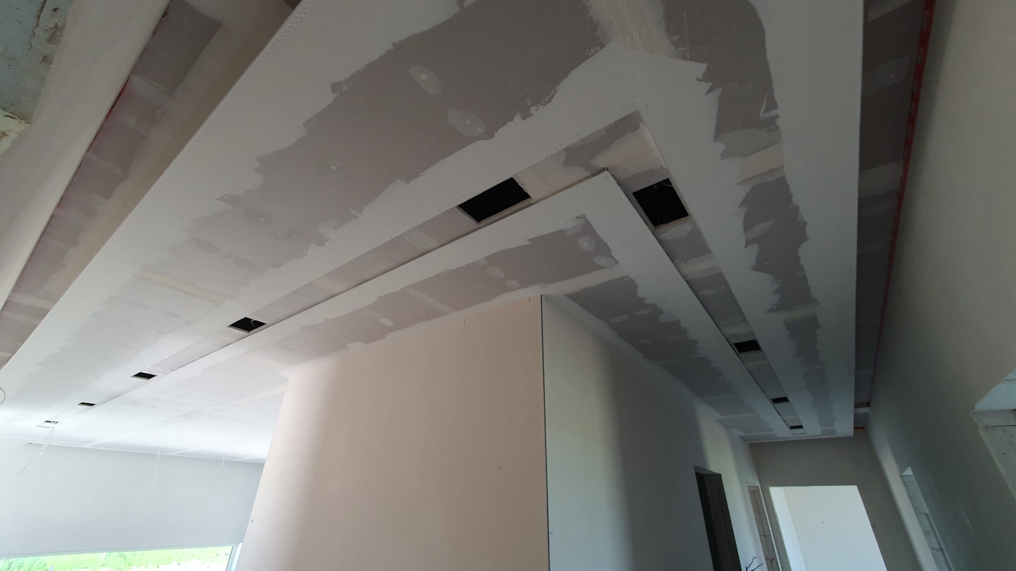 Sufit podwieszany z płyt kartonowo-gipsowych w trakcie szpachlowania, widoczne otwory na oświetlenie, ślady szpachli na łączeniach płyt.