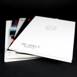 Stos teczek ofertowych z logo PB Nails Nederland na białym tle, ułożonych na czarnym tle, widoczne inne materiały reklamowe w tle.