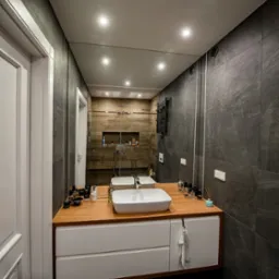 Nowoczesna łazienka z szarymi płytkami, drewnianym blatem pod umywalką nablatową i dużym lustrem, w którym odbija się kabina prysznicowa z drewnianymi akcentami.