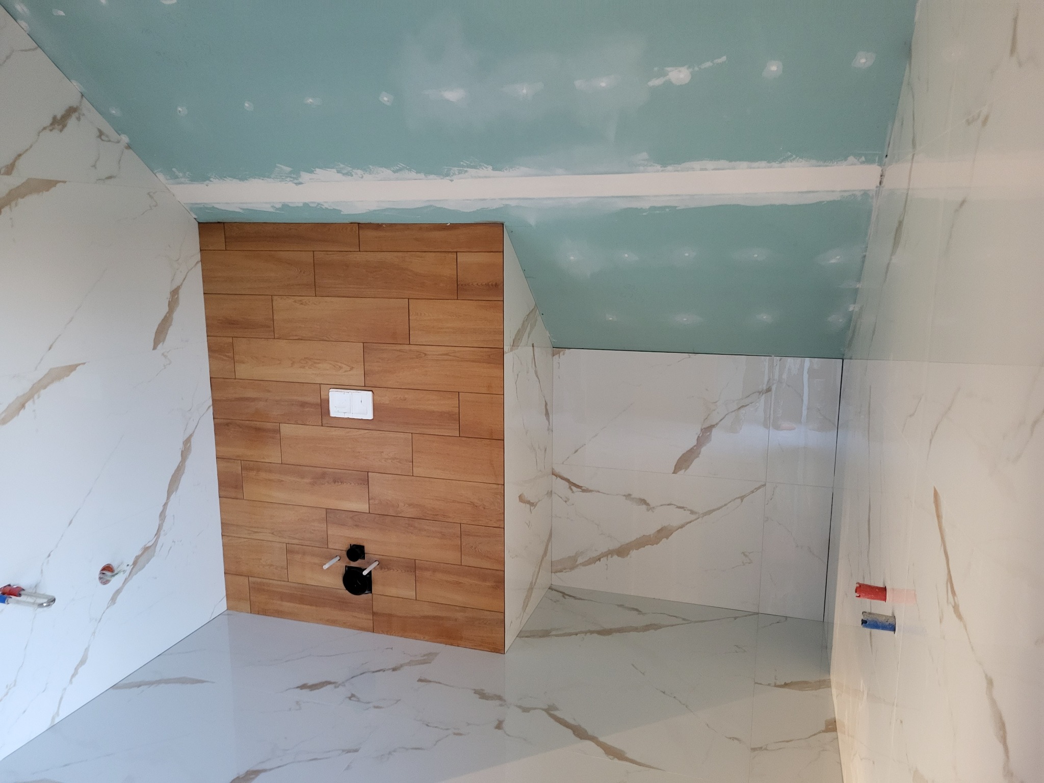 Łazienka w trakcie wykańczania: połączenie płytek imitujących drewno i marmur, sufit z widocznymi śladami szpachlowania.