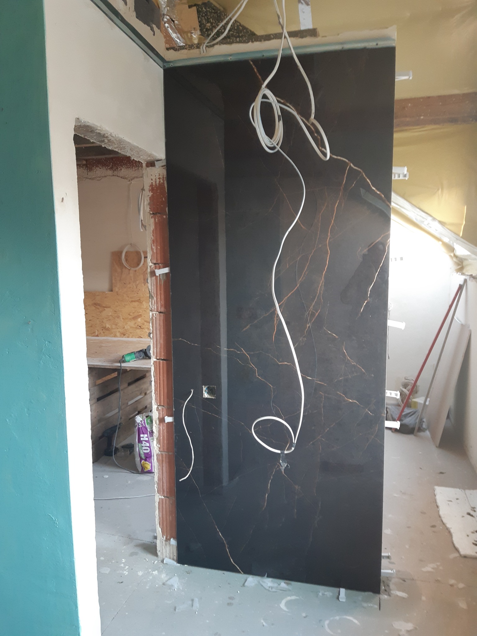 Ciemna, błyszcząca płyta z marmurowym wzorem, częściowo zamontowana w ościeżnicy, z widocznymi przewodami elektrycznymi i elementami konstrukcyjnymi w tle.