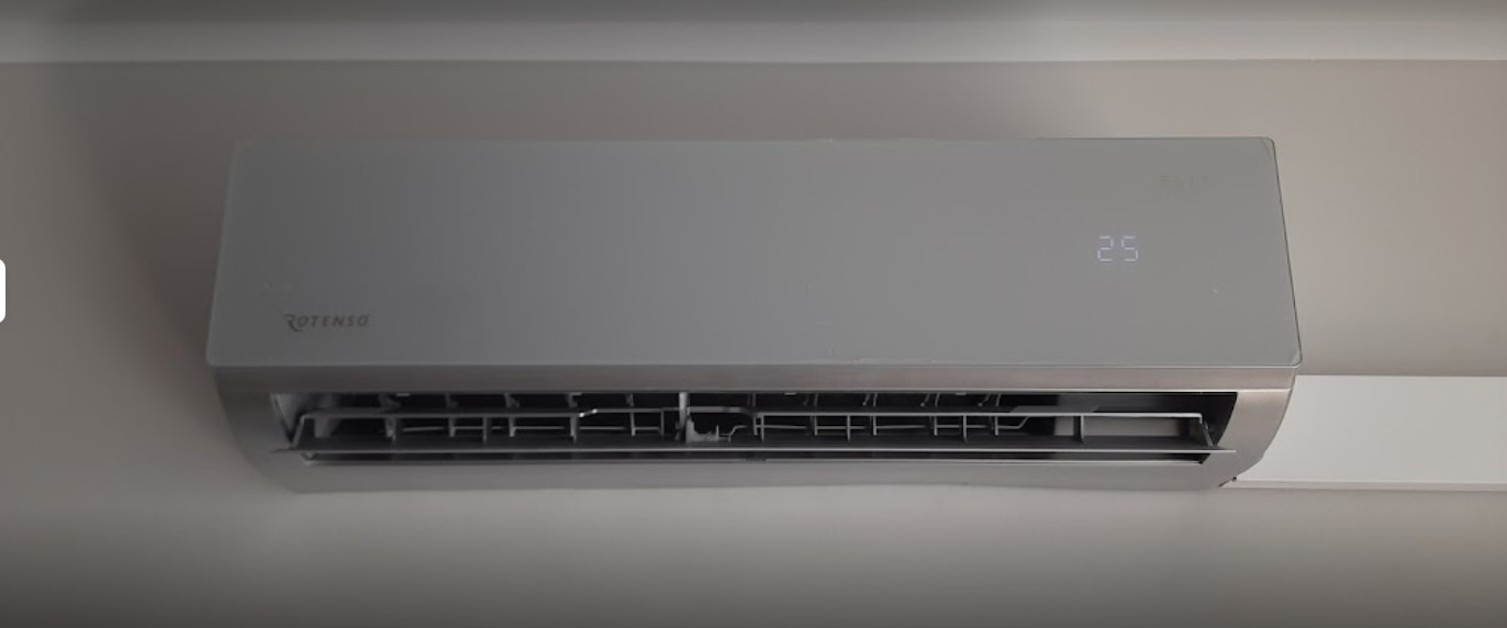 Szara klimatyzacja Rotenso z wyświetlaczem temperatury 25 stopni Celsjusza, zamontowana na ścianie w pomieszczeniu.