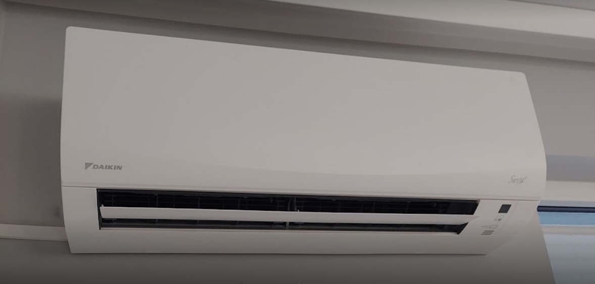 Biała jednostka klimatyzacyjna Daikin Seria zamontowana na szarej ścianie w pomieszczeniu.