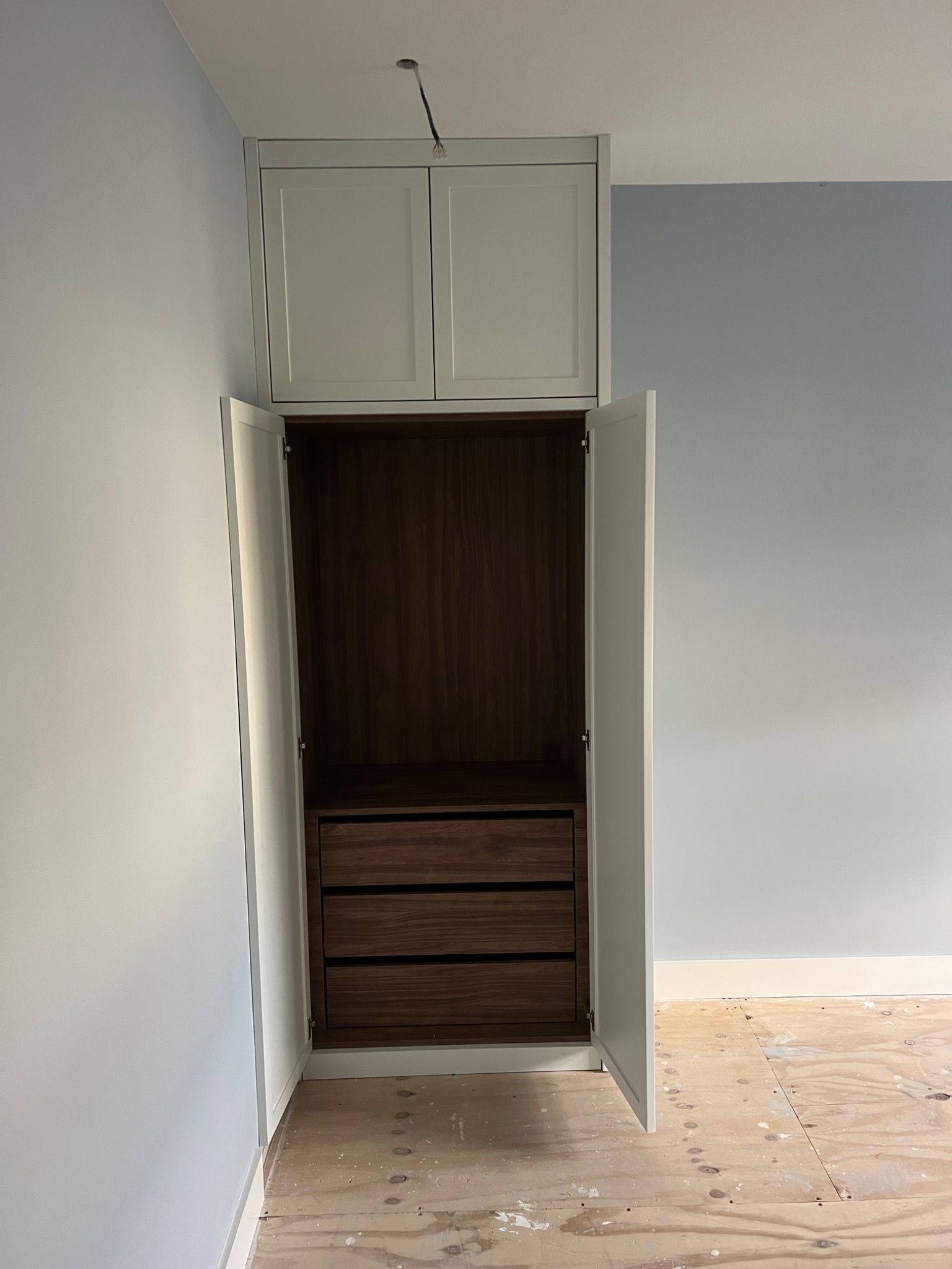 Wnętrze szafy wnękowej z trzema drewnianymi szufladami, białe fronty szafy, surowa podłoga w tle, widoczne niedokończone wykończenie wnętrza.